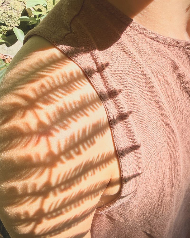 The shadow of a fern frond falling across a shoulder in warm afternoon light.