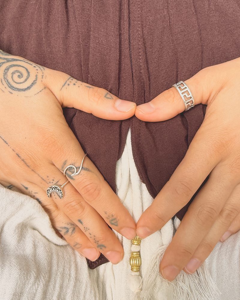 Two hands resting low over the belly, fingers meeting in a downward triangle.